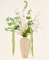Un bouquet de fleurs artificielles en soie, Crystal Garden, composé de fleurs blanches et vertes et de feuilles suspendues dans un grand vase beige avec structure.