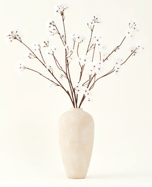 Le bouquet de fleurs artificielles en soie Fleur de cerisier crème 114 cm se dresse haut dans un vase en céramique beige et apporte une décoration sereine à n'importe quelle pièce avec ses délicates branches de couleur crème sur un fond clair.