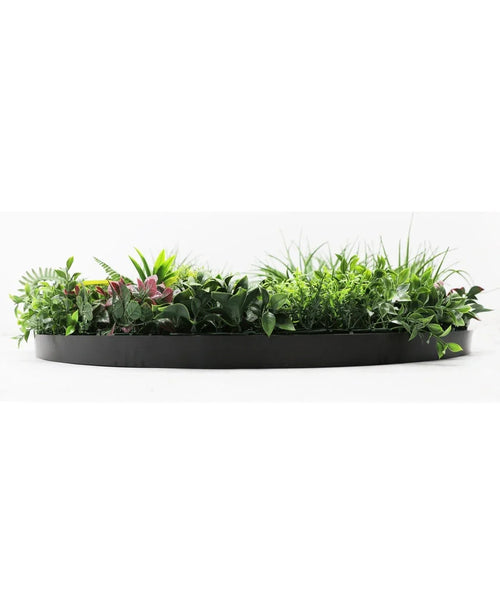 La Haie Artificielle sur Cadre Noir Ø100 cm est une jardinière noire semi-circulaire remplie d'un feuillage vert luxuriant et de quelques feuilles teintées de rose, sur un fond blanc.