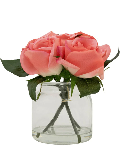 Le bouquet de roses artificielles Real Touch Pink 18 cm comprend quatre roses artificielles roses aux feuilles vertes, disposées dans un petit pot en verre et sur un fond blanc.