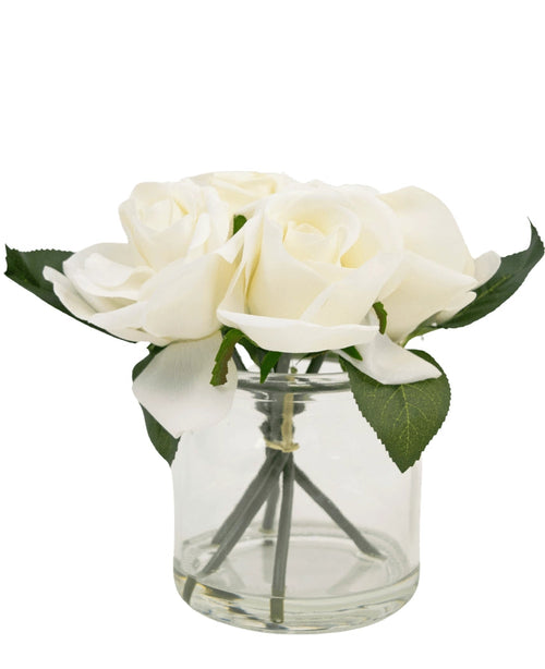 Le Bouquet de Roses Artificielles Real Touch Blanc 18 cm est un petit vase en verre avec plusieurs roses artificielles blanches et feuilles vertes, joliment disposées sur un fond blanc uni.