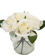 Le Bouquet de Roses Artificielles Real Touch Blanc 18 cm est un petit vase en verre transparent avec des roses blanches et des feuilles vertes réalistes, sur un fond blanc uni.