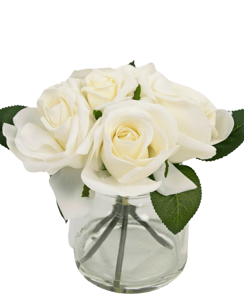 Le Bouquet de Roses Artificielles Real Touch Blanc 18 cm est un petit vase en verre transparent avec des roses blanches et des feuilles vertes réalistes, sur un fond blanc uni.