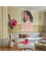 Un salon moderne avec un canapé modulable, un arrangement floral rose d'herbe à chat artificielle (75 cm) dans un vase, un plaid moelleux et une peinture murale abstraite représentant une femme. L'intérieur se caractérise par des couleurs douces et des accents à motifs.