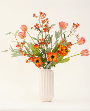 Het Zijden kunstbloemen boeket Orange Glory, met oranje tulpen, klaprozen en groene bladeren, is prachtig gerangschikt in een vaas met witte textuur tegen een effen lichte achtergrond.