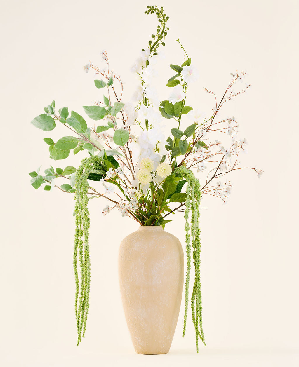 Un bouquet de fleurs artificielles en soie, Crystal Garden, composé de fleurs blanches et vertes et de feuilles suspendues dans un grand vase beige avec structure.