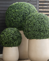 Trois grands pots de buis artificiels de style romain UV D65 cm présentent des topiaires vertes sphériques soigneusement taillées sur un fond de lattes de bois sombre sur un plancher en bois.