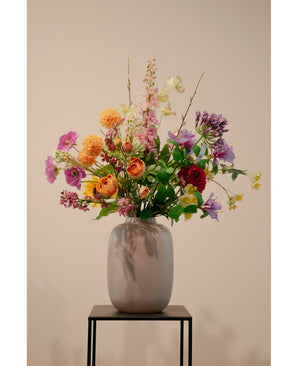 Een Kunst Klaproos Real Touch Paars 65cm staat in een vaas van wit keramiek. De levensechte paarse bloemen staan op een zwart metalen standaard tegen een effen beige achtergrond.