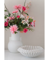 Een witte vaas met een Kunstbloem Rododendron Azalea 73 cm fuchsia staat naast een witte schaal van geribbeld keramiek op een effen ondergrond tegen een neutrale achtergrond.
