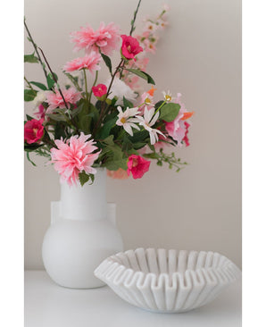 Een Kunstbloem Dahlia 68 cm roze in een witte vaas staat naast een schaal van wit keramiek met ruches op een wit oppervlak, tegen een effen lichte achtergrond.