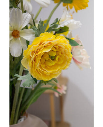 Een close-up van de Kunstranonkel Real Touch Geel 60cm, een levendige gele kunstranonkel met gelaagde bloemblaadjes, geschikt in een vaas binnenshuis naast witte en lichtroze bloemen.